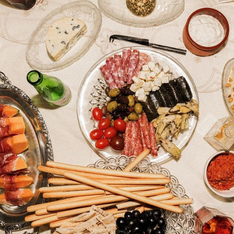 A table laid out with an assortment of meze dishes including cured meats, cheese, fruit, bread and dips. Some drinks can also be seen.