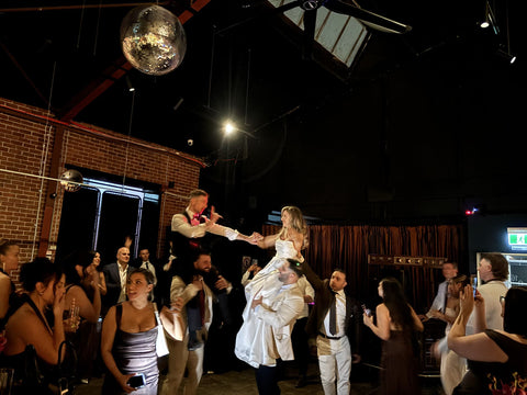 Bride and groom lifted on guests' shoulders on the dance floor at Three Foxes Distillery warehouse wedding venue. Cocktail party, the party doesn't stop.